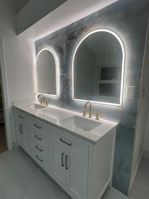 High-end dual vanity bathroom with white cabinetry, marble backsplash, and modern LED-backlit arched mirrors