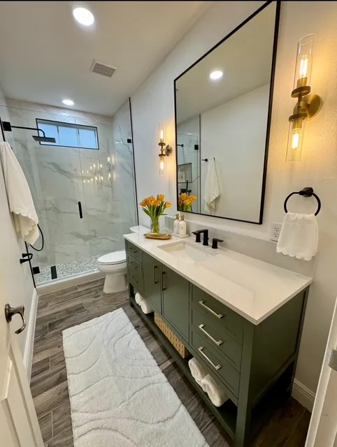 Charming guest bathroom with sage green vanity, marble shower surround, black fixtures, and elegant mirror