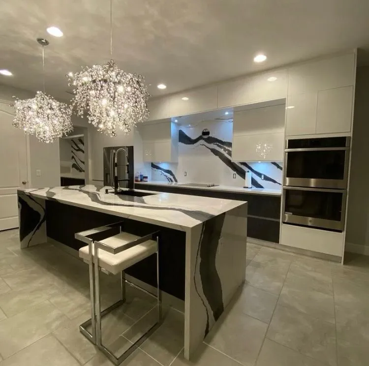 High-end kitchen featuring marble waterfall island, crystal chandeliers, and premium appliances with artistic backsplash