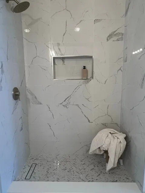 Luxury shower interior with marble walls, built-in niche, rainfall showerhead, and towel storage bench