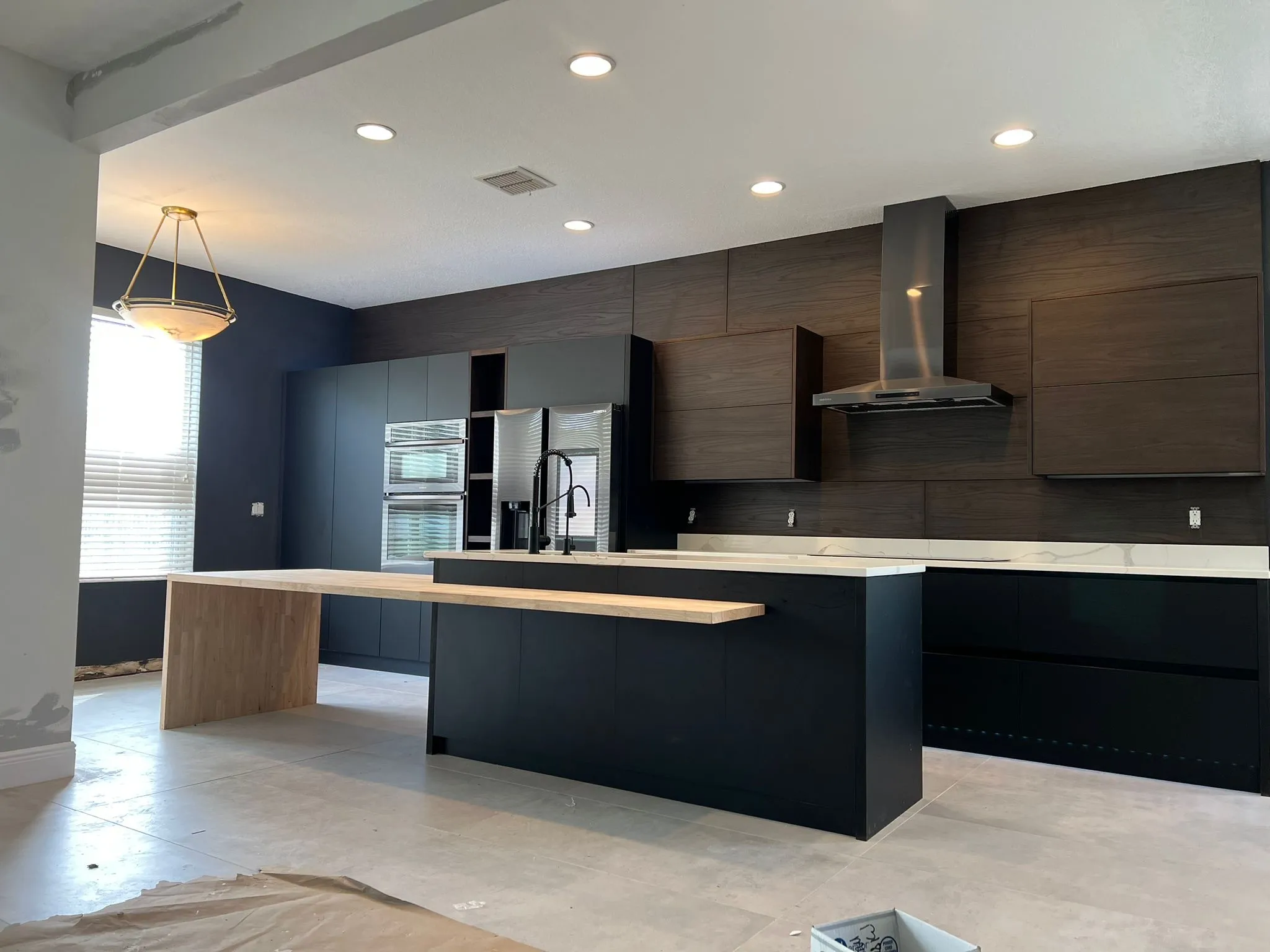 Contemporary kitchen featuring navy blue lower cabinets, wood-grain upper cabinets, white countertops, and elegant gold geometric pendant lighting