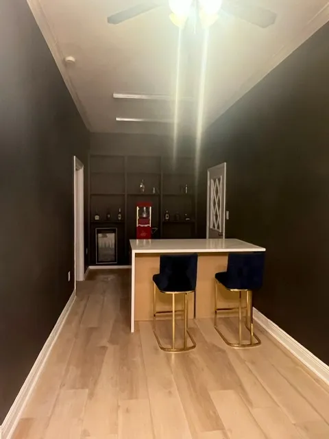Sophisticated wet bar area with dark walls, white waterfall countertop, gold bar stools, and modern lighting