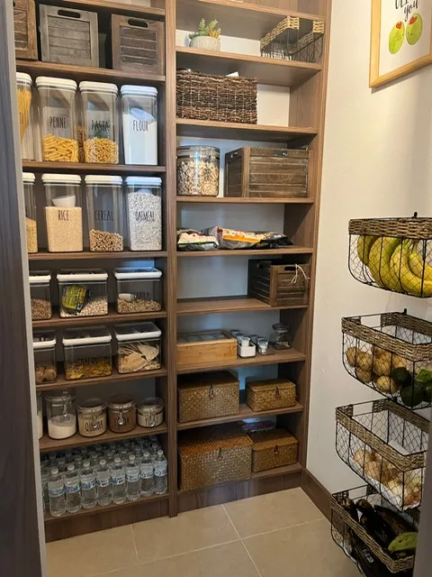 Beautifully organized pantry with custom wood shelving, featuring clear storage containers, wicker baskets, and efficient storage solutions with marble tile flooring