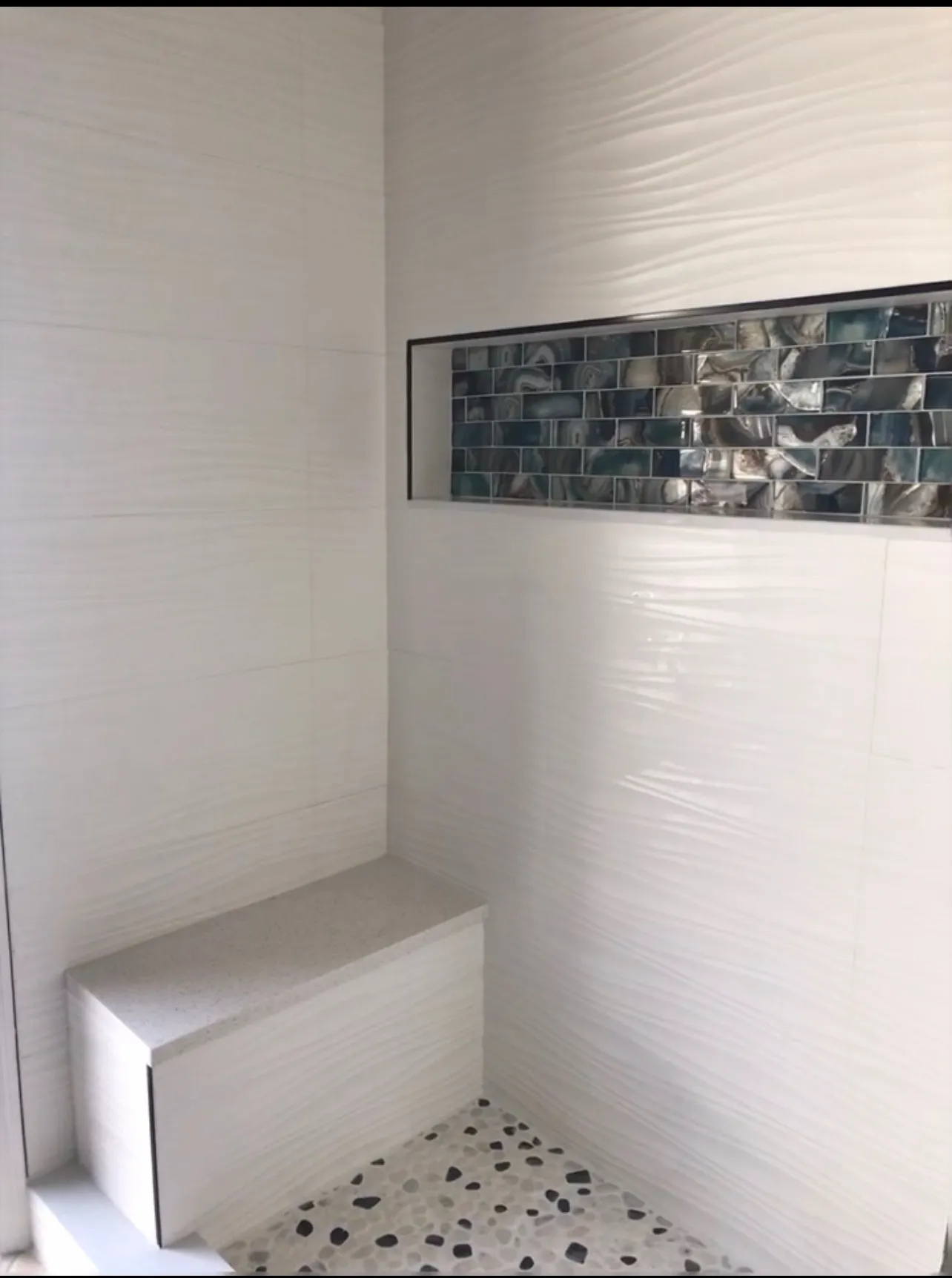 Luxury shower interior with marble walls, built-in bench seating, decorative niche, and premium fixtures
