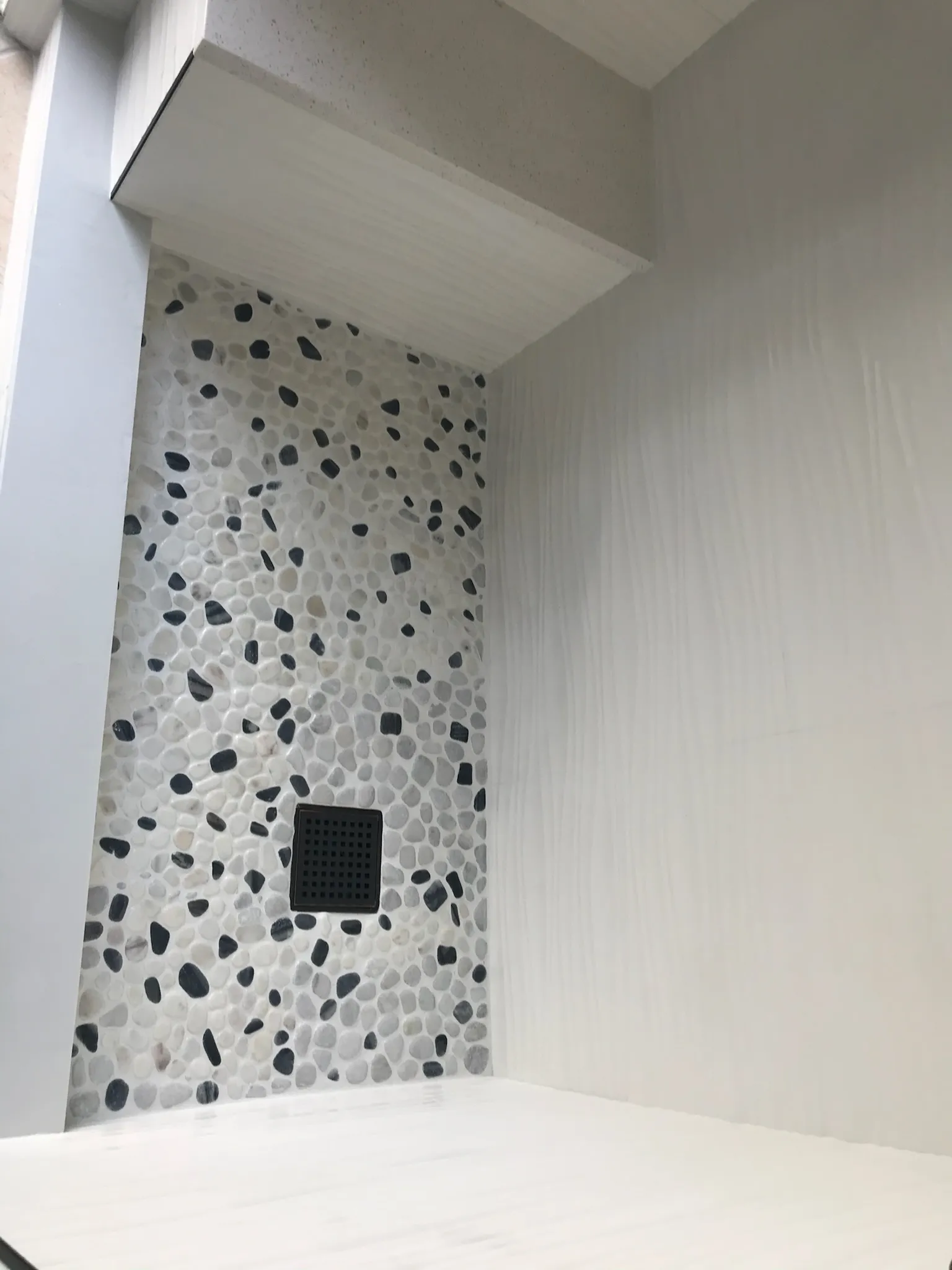 Detailed view of shower niche with decorative pebble tile accent and modern built-in storage