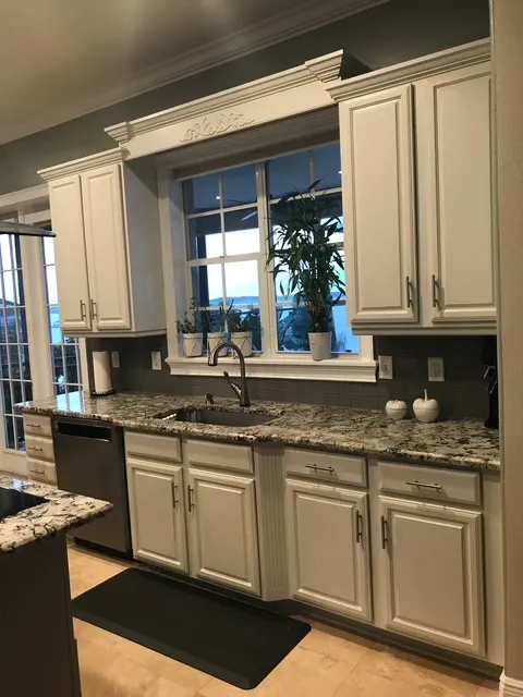 Traditional kitchen featuring white cabinetry, granite countertops, and large window over sink area
